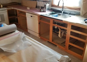 Kitchen cabinetry with cabinet doors removed and surfaces covered, showing preparation stage for cabinet refinishing in Wilmington
