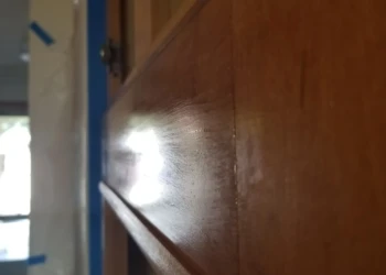 Close-up of wood cabinet door surface with visible grain texture and light reflection