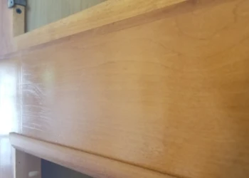 Close-up view of a natural wood cabinet door with visible varnish brush strokes and wood grain texture