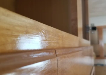 Close-up of glossy wood cabinet edges displaying smooth finish and natural wood grain with visible hinge in a residential kitchen