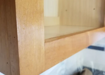 Close-up view of a wooden kitchen cabinet corner showing varnish finish with light wood grain