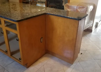 Close-up of kitchen cabinets with glossy dark granite countertop showing dull and uneven finish in Wilmington kitchen