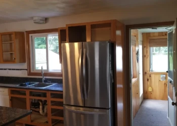 Unfinished kitchen cabinets surrounding a stainless steel refrigerator and black granite countertop in Wilmington MA kitchen