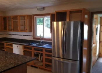 Kitchen with cabinets stripped of doors and drawers around stainless steel refrigerator and granite counters ready for cabinet refinishing Wilmington