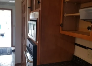 Close-up of kitchen cabinets with warm wood finish and some doors open showing shelves, in a Wilmington, MA home