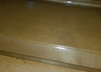 Close-up photo showing smooth wooden cabinet surface with visible finish imperfections before refinishing