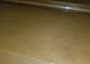 Close-up of the worn and peeling varnish on a cabinet surface showing prior low-quality refinishing work