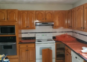 Kitchen cabinets with glossy varnished wood doors and black knobs surrounding white stove and microwave in Wilmington