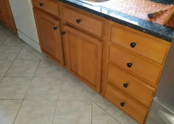 Close-up of wood kitchen cabinets and drawers under a dark granite countertop near a stainless steel appliance