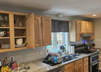 Wooden kitchen cabinets with natural finish above and below a granite countertop with kitchen sink and dishwasher in Windham NH