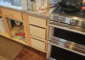 Light wood kitchen cabinets with drawers removed next to stainless steel stove and granite countertop in Windham NH