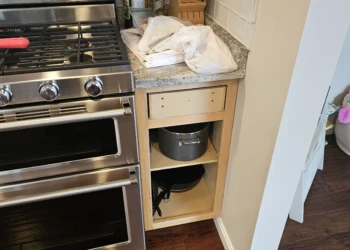 Stripped and partially disassembled wooden kitchen cabinet next to stainless steel stove with countertop items in Windham NH