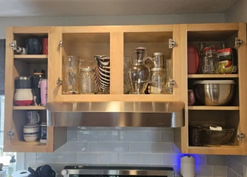 Open wooden kitchen cabinets above stove showing stripped bare wood surfaces during cabinet refinishing project in Windham NH