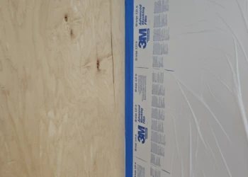 Close-up of bare wood cabinet surface next to taped protective sheet during cabinet refinishing in Windham NH