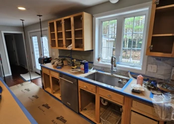 Kitchen cabinets in Windham NH stripped down with doors removed and blue painter's tape along countertops during cabinet refinishing preparation