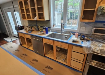 Bare wood kitchen cabinets with doors removed and taped countertop during cabinet refinishing in a Windham NH kitchen