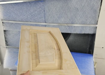 Hand holding a stripped and sanded wooden cabinet door panel in a workshop