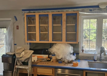 Kitchen cabinets taped and covered with plastic during preparation phase of cabinet refinishing project in Windham NH