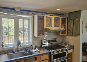 Kitchen cabinets stripped down and protected with masking tape and coverings during cabinet refinishing preparation in Windham NH