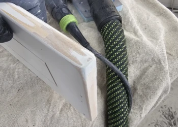 Sanded cabinet door edge held next to a Festool sander tool on a cloth surface during cabinet refinishing in Windham NH