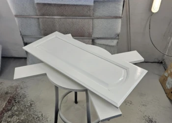Primed cabinet door resting on wooden boards supported by stool in refinishing workshop