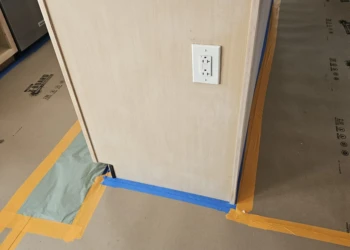 Close-up of a primed kitchen island cabinet side with electrical outlet and protective floor covering in Windham NH