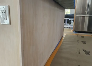 Bare wood cabinet surfaces stripped and prepped with painter's tape along the baseboard in a Windham NH kitchen