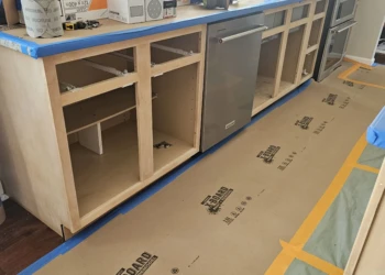 Kitchen cabinets stripped down to bare wood and prepped for refinishing around a dishwasher and stove