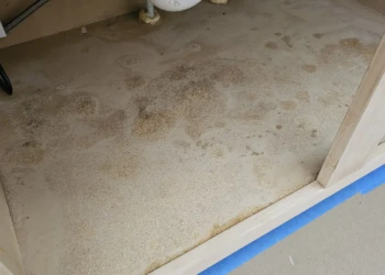 Inside cabinet base showing stripped and sanded wood surface with plumbing pipes above during cabinet repair in Windham NH