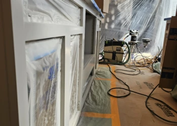 Close-up of white cabinet frames during finishing stage with protective plastic and painting equipment in Windham NH