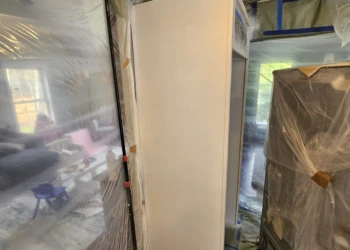 Freshly refinished white cabinet side surrounded by protective plastic sheeting during cabinet refinishing project in Windham NH