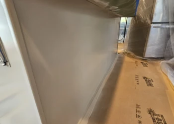 Close-up of freshly refinished kitchen cabinet baseboard with protective coverings on floor and surrounding area in Windham NH
