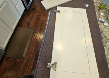 Painted white cabinet doors and drawer front neatly laid on padded surface in a kitchen during cabinet refinishing