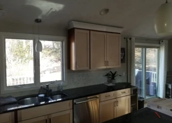 Kitchen cabinets being refinished with a spray gun in a modern kitchen.