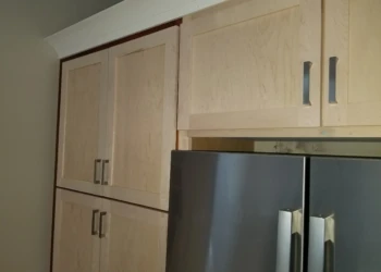 Kitchen cabinet refinishing project with light wood cabinets and stainless steel appliances.