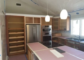 Kitchen cabinets being refinished with sanding and masking for painting.