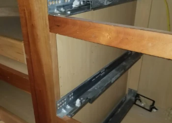 Close-up of cabinet drawer slides being installed in a wooden cabinet frame.