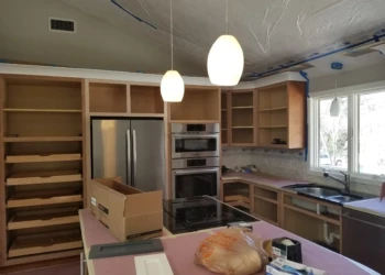 Kitchen cabinet refinishing in progress with open cabinets and tools.