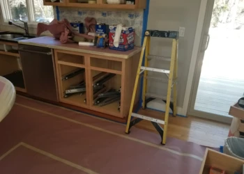 Refinishing cabinets in a kitchen with tools and ladder nearby.