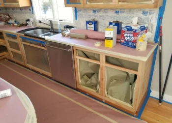 Kitchen cabinets being refinished with protective paper and masking tape.