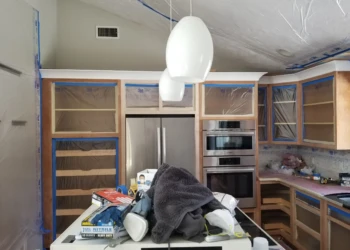Kitchen cabinets being refinished with protective masking and sanding tools.