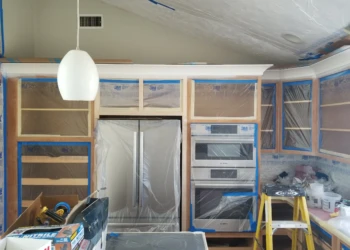 Kitchen cabinets being refinished with protective masking and plastic wrap.