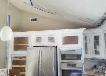 Kitchen cabinets being refinished with protective plastic and masking tape.