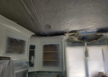Kitchen cabinets being refinished with protective plastic covering the surrounding area.