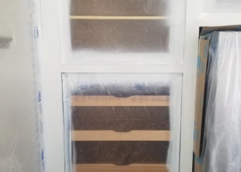Cabinet refinishing in progress with protective plastic covering.