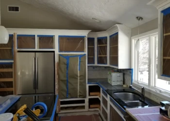 Kitchen cabinets being refinished with protective tape and plastic covering.