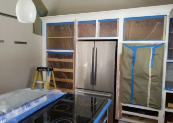 Kitchen cabinet refinishing with masking tape and plastic covering.