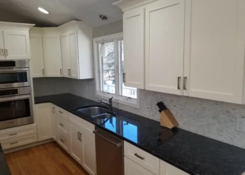 Kitchen cabinets being refinished with a black countertop and white cabinets.