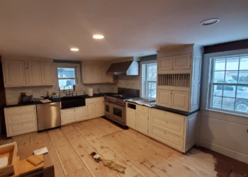Kitchen with white cabinets, black granite countertops, stainless steel appliances, and unfinished wood plank flooring in Amherst, NH