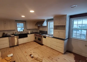 Wide view of cream-colored kitchen cabinets with black countertops and stainless steel appliances in Amherst NH kitchen